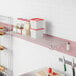 A Regency stainless steel wall-mount wire shelf in a kitchen with clear containers on it.