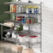 A Regency stainless steel wall-mount shelf post with single brackets holding food items on a wire shelf.