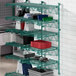 A green metal Regency wall-mounted shelf with dishes and pots on it.