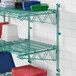 A green Regency wire shelf with dishes and plastic containers on it.