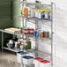 A metal Regency wall-mount shelf with food containers on it.