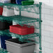 A green Regency wall-mount shelf with blue and grey plastic bins on it.