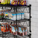 A Regency black wire wall shelf with snacks and drinks on it.