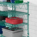 A Regency green metal wall-mount wire shelf with plastic containers on it.