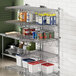 A Regency stainless steel wall-mount shelf post with a shelf and containers on it in a professional kitchen.