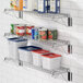 A Regency stainless steel wall-mount wire shelf holding white and blue food containers and cans.
