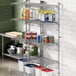 A Regency wall-mount wire shelf post in a professional kitchen with shelves filled with food.