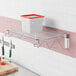 A Regency stainless steel wall-mount wire shelf with a white and red container on it.
