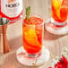 A glass of red NOROI Esprit-d'Italie non-alcoholic aperitivo with a sprig of rosemary and a slice of orange.