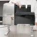 A person in a white coat using a Hobart LIFT-KNIT unit to cut meat.