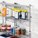 A Regency chrome wall-mounted wire shelf with food cans and containers on it.