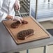 A chef cutting a piece of meat on a San Jamar Tuff-Cut grooved cutting board.