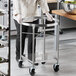 A person in a kitchen with a Choice stainless steel mixing bowl stand with locking casters.