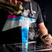 A man using a Flavour Blaster to pour blue liquid into a plastic cocktail glass.