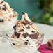 A close-up of a bowl of ice cream topped with English toffee pieces and flaked chocolate.