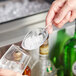 A person using a Visions clear disposable utility scoop to add ice to a glass.