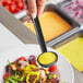 A person using a Choice black polycarbonate serving ladle to serve salad
