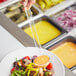 A person using a Choice clear polycarbonate serving ladle to serve salad