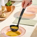A person using a Visions black plastic ladle to serve soup.