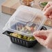 A hand holding a black Ecopax plastic take-out container with food inside.