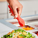 A person holding red Choice flat grip tongs over a salad.