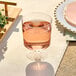 A Visions clear plastic wine cup filled with pink liquid on a table.