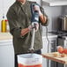 A man in a chef's uniform using a Galaxy medium-duty immersion blender in a professional kitchen.