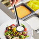 A person holding a Choice black polycarbonate serving ladle over a bowl of salad.