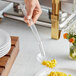 A hand holding a Choice clear polycarbonate perforated salad bar spoon filled with yellow corn over a plate of food.