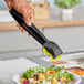 A hand using black polycarbonate salad tongs to serve salad