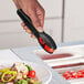 A person using a Choice black polycarbonate scallop grip tong to serve tomatoes.