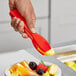 A hand using Choice red polycarbonate salad tongs to serve fruit