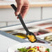 A person holding a Choice black polycarbonate salad bar spoon over a bowl of salad.