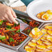 A person holding a clear plastic Visions spatula over food on a table.