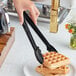 A person using Choice black polycarbonate scallop grip tongs to serve a waffle.