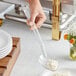 A person using a Choice clear polycarbonate salad bar spoon to serve food on a plate.