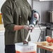 A man in a chef's uniform using a Galaxy medium-duty immersion blender on a counter in a professional kitchen.