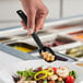 A person holding a Choice black polycarbonate salad bar spoon over a plate of food.