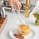 A person using Choice clear polycarbonate tongs to serve a stack of pancakes and sausages.