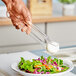 A hand using Choice clear polycarbonate flat grip tongs to serve salad