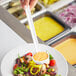 A person using a Choice white polycarbonate serving ladle to put sauce on a bowl of salad.