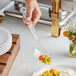 A person holding a Choice clear polycarbonate perforated salad bar spoon full of vegetables over a table of food.