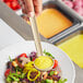 A person using a Choice beige polycarbonate serving ladle to serve salad