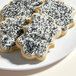 Three sugar cookies with white frosting and Adourne black sparkling sugar on a white plate.