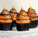 A white cake stand with five cupcakes with chocolate and orange frosting and Adourne Coarse Black Sanding Sugar on top.