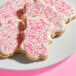 A plate of sugar cookies decorated with white icing and coarse pink sanding sugar.