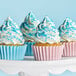 A white cake stand with a cupcake topped with white frosting and blue sprinkles on it.