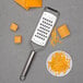 A Microplane extra-coarse cheese grater on a plate of cheese cubes.