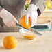 A person grating an orange with a Microplane Classic zester blade over a bowl.