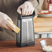 A person using a Microplane Elite stainless steel box grater to grate cheese.
